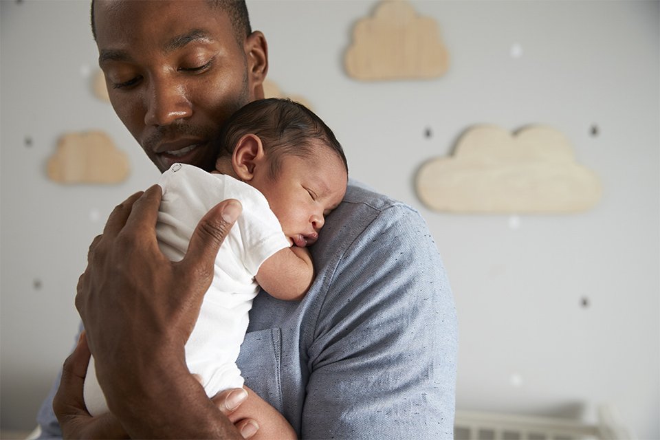 A father holding a newborn in a nursery.